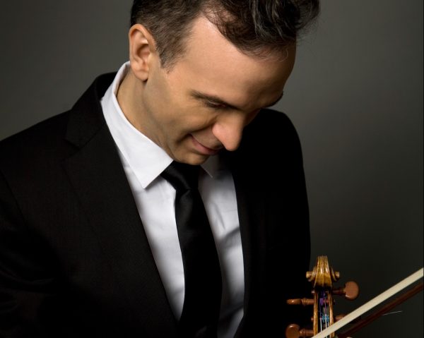 A man in a suit looks down at a violin.