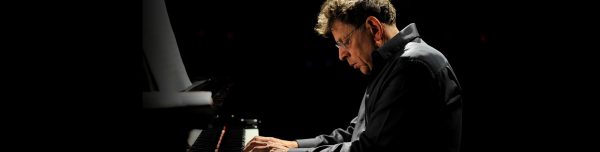 Philip Glass, composer, sits at a piano.