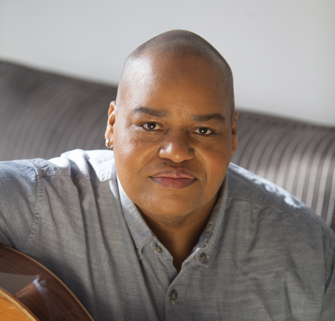 Toshi Reagon sits with a guitar on her lap wearing a denim button down shirt.