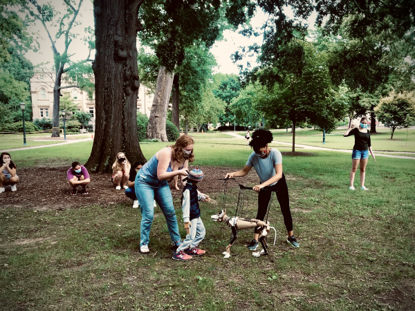 Two women stand outside on UNC's quad holding puppets on long strings as they rehearse for an opera.