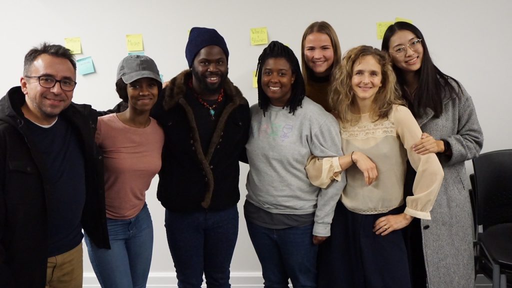 seven people pose for a photo together in front of a white wall with yellow post-it notes bearing handwriting