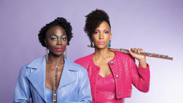 Flutronix artists Nathalie and Allison stand wearing brightly colored clothes and holding their flutes.