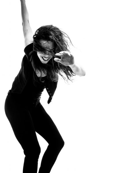 Dancer Michelle Dorrance smiles while tapping, her arms up in the air.