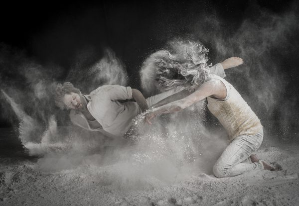 Two dancers, Tommy and Murielle, strike dramatic poses while all-purpose flour flies around them, creating a white, cloudy smoke.