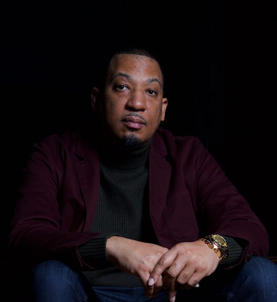 A man looks directly at the camera, wearing a watch.
