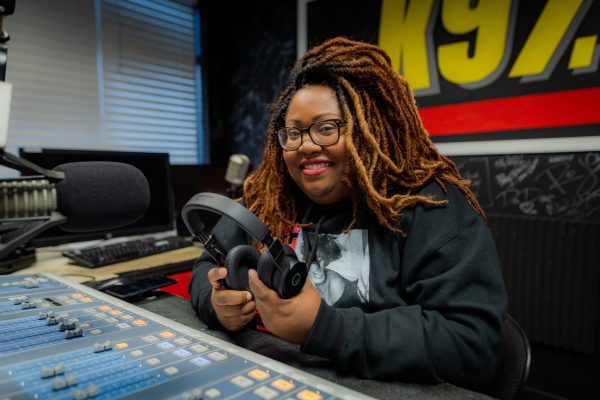 A woman smiles while holding headphones.