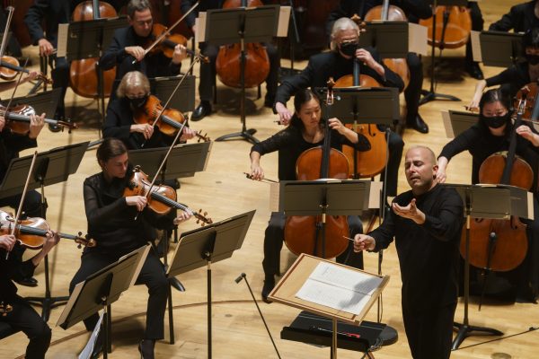An orchestra performs with various instruments, led by a conductor. They are dressed in black.