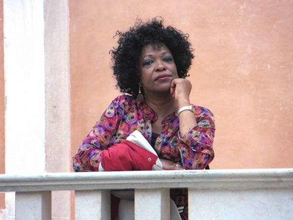 A woman stands on a balcony, a jacket in hand.