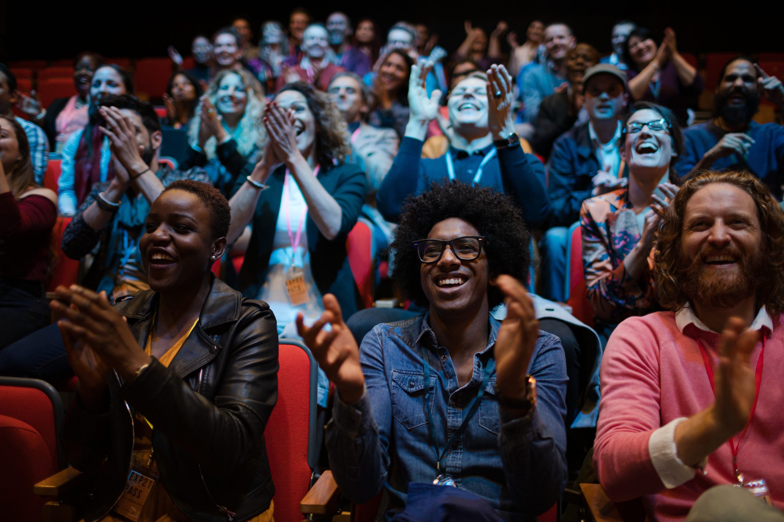 A crowd of theatergoers laughing and applauding during a live performance