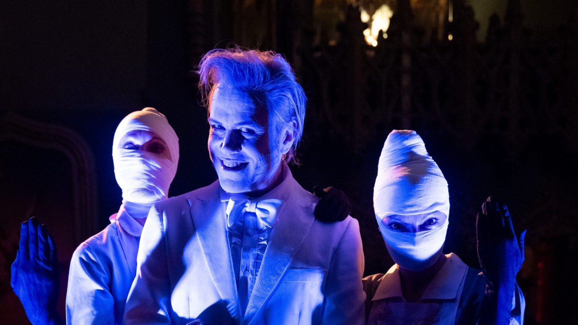Performers in white suits and white-wrapped masks, lit in deep blue, inside the immersive BARDO experience