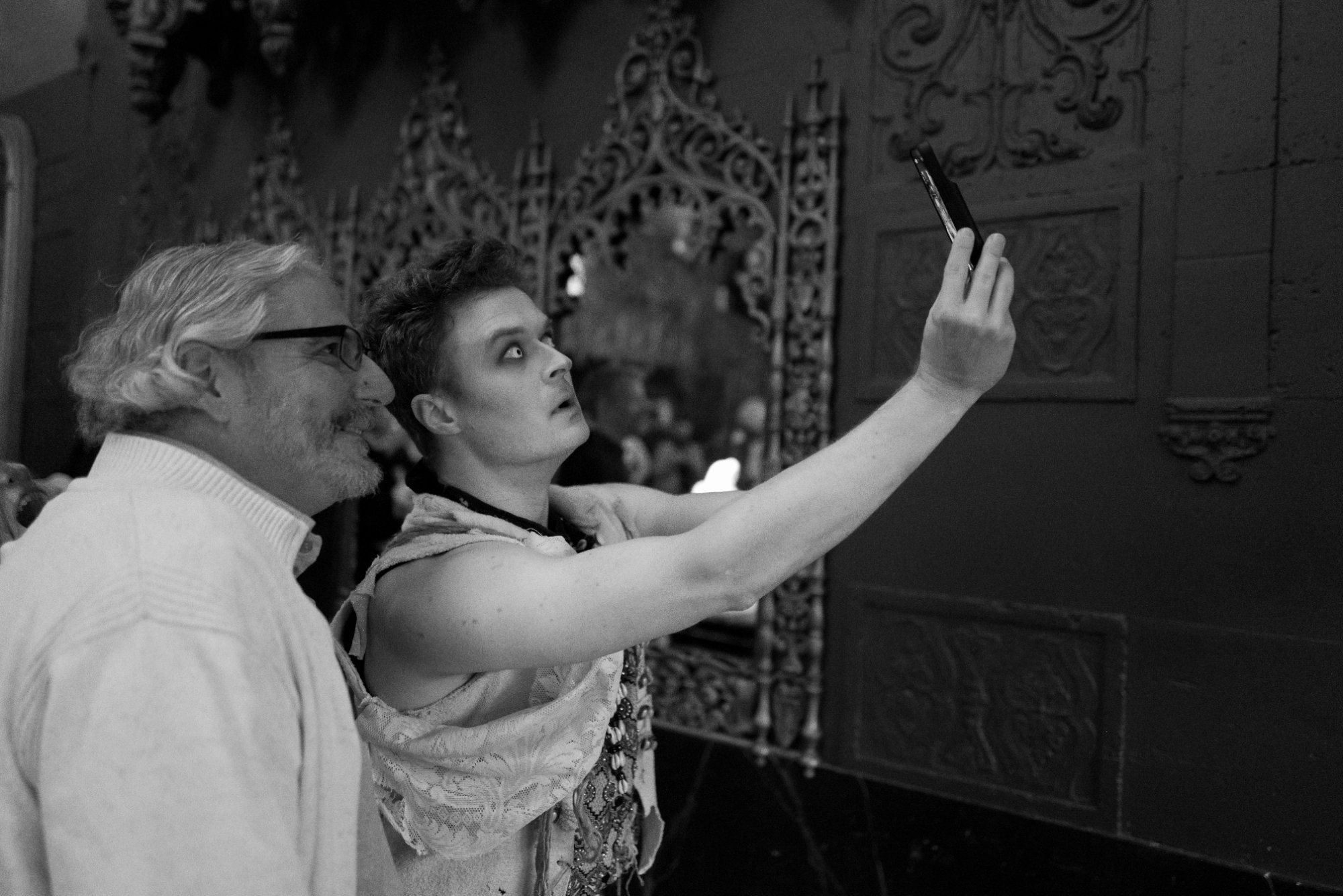 Black-and-white photo of a costumed performer taking a selfie with an audience member during BARDO