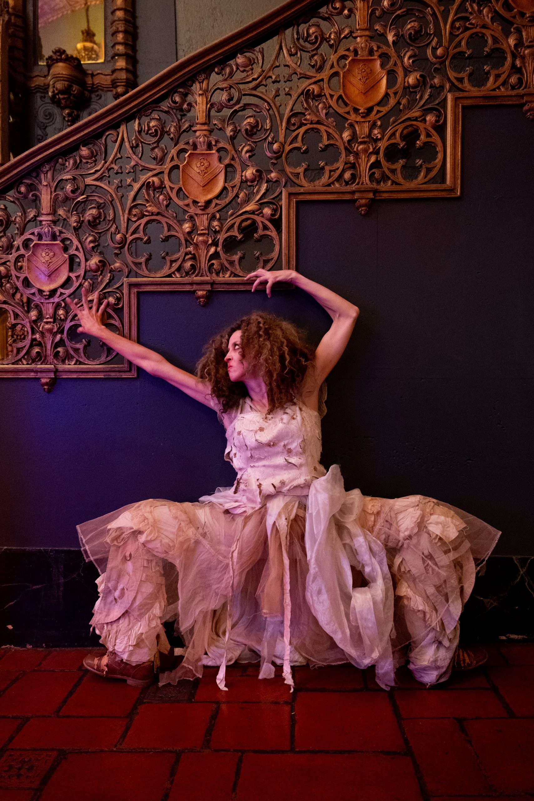 A hungry ghost in a tattered white gown sprawls at the foot of an ornate staircase