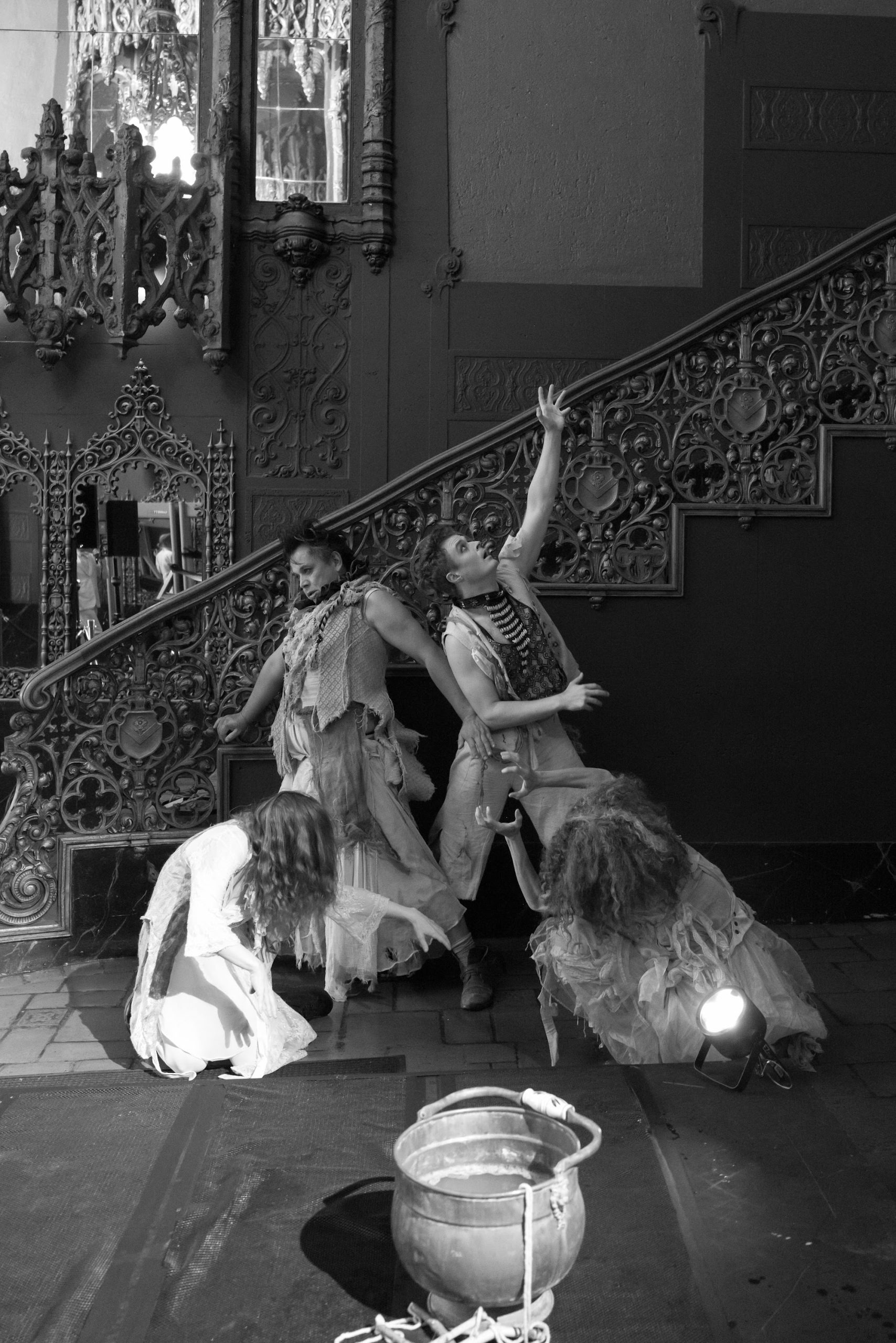 Black-and-white photo of three hungry ghosts in ragged gowns posed on a grand staircase
